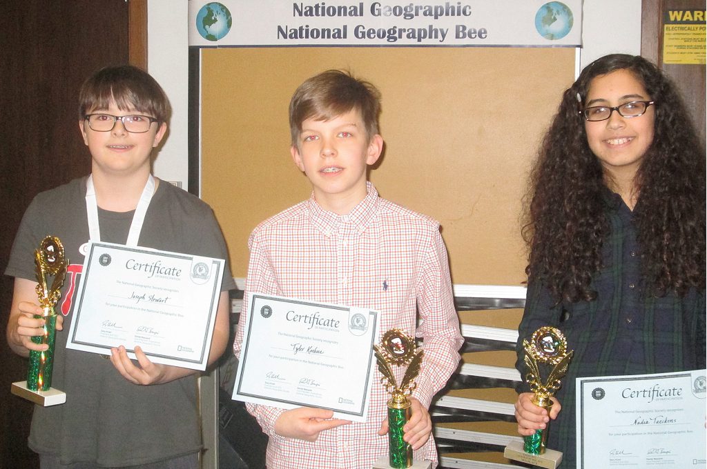 Three students holding certifcates and trophies. 