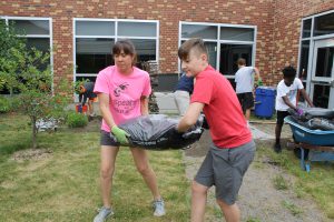 A student and staff member carrying a bag of mulch. 