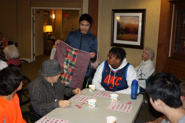 A male student holds up a quilt so a resident can see it better.