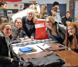 This is an image of five F-M High School students sitting at desks, smiling and wrapping gifts