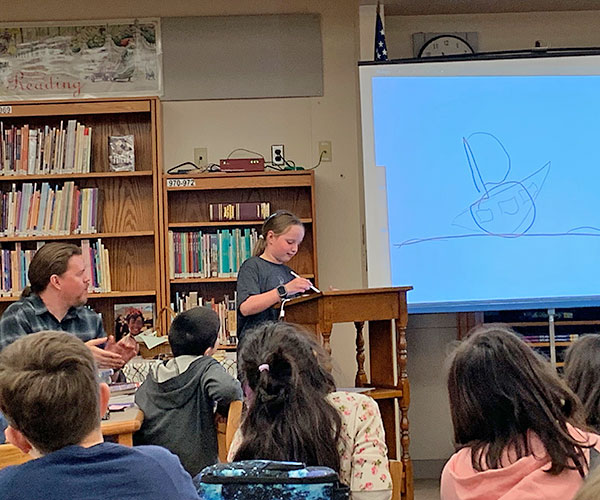 This is an image of a student drawing while author Nathan Hale talks to students