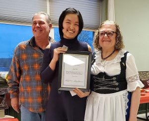 A female student holds a certificate while a man stands on her right and a woman is on her right. 