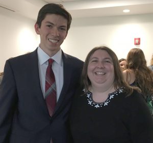 A male student stands next to a female teacher. 