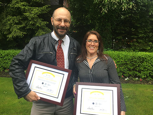 A man and woman standing side-by-side holding framed diplomas. 