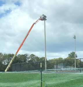 A boom lift stretches to the top of a stadium light post. 