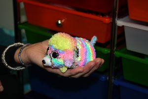 Small rainbow colored stuffed animal held in the palm of a hand. a