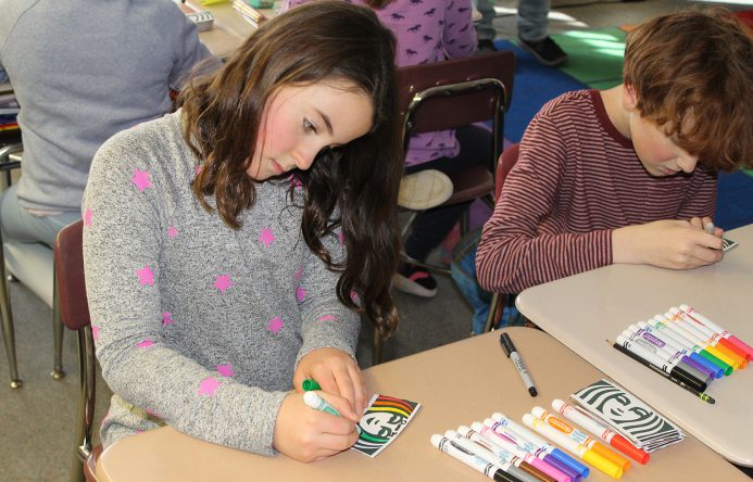 Girl and boy seated at desks coloring.