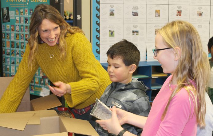 Teacher handing girl coffee sleeves; boy standing between them.