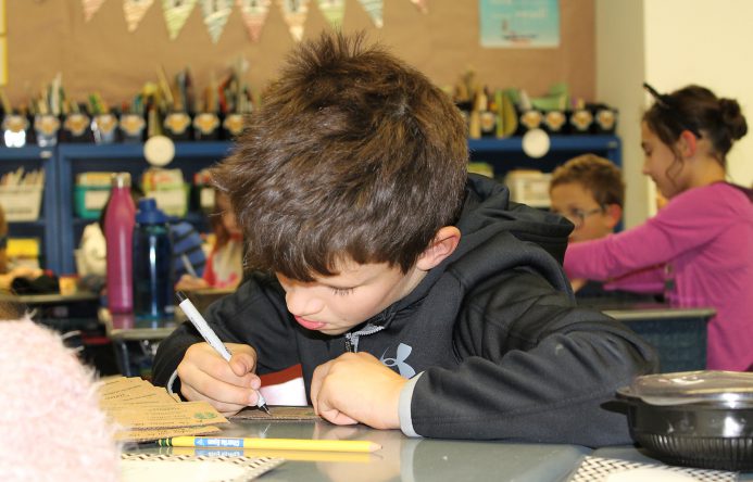 Boy seated at desk writing.