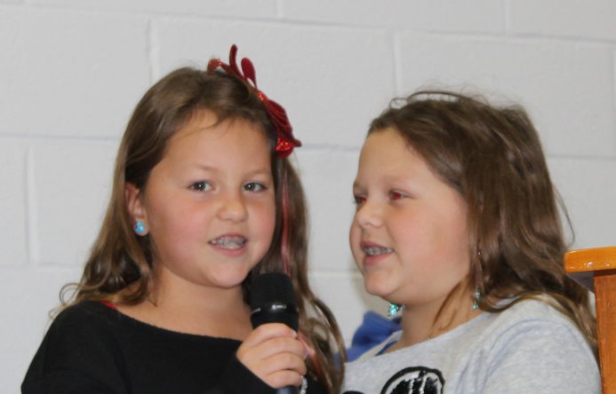 Two girls, both holding and talking into a microphone.