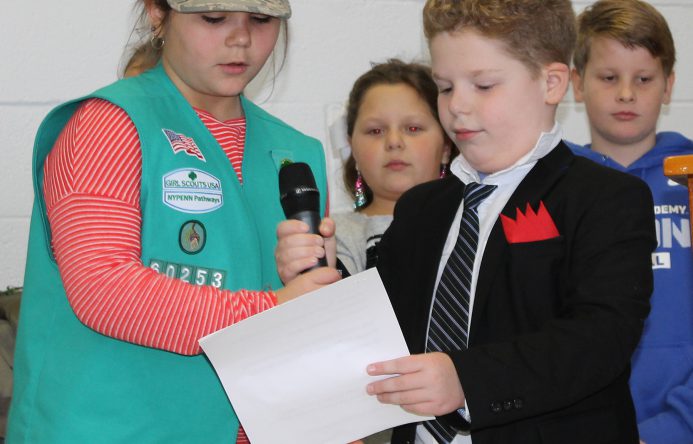 Girl, left, wearing army cap, and boy, right, holding piece of paper they are both reading from.