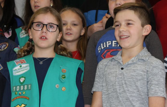 Girl. left and boy, right, standing while singing.