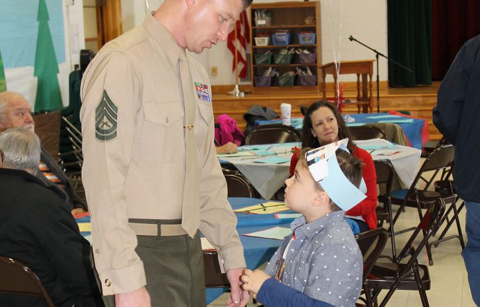 Man in uniform, left, standing by boy, right, touching hands.