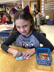 Girl smiles at camera while decorating a paper quilt square.