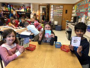 Three students, seated, holding up their decorated paper quilt squares.