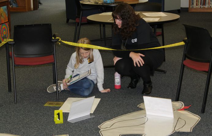 Teacher talking to student who is seated on floor.