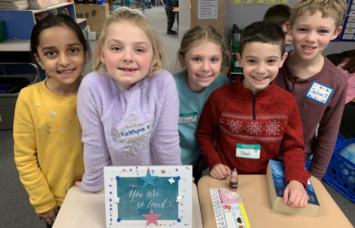 Students standing behind desk with decorated frame on desk.