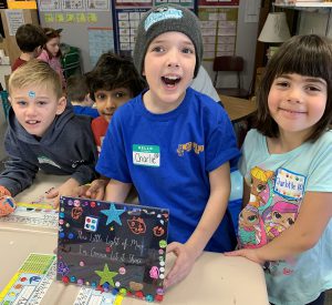 Students standing behind desk with decorated frame on desk.