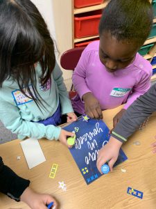 Students standing behind desk with decorated frame on desk.