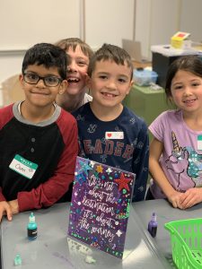 Students standing behind desk with decorated frame on desk.