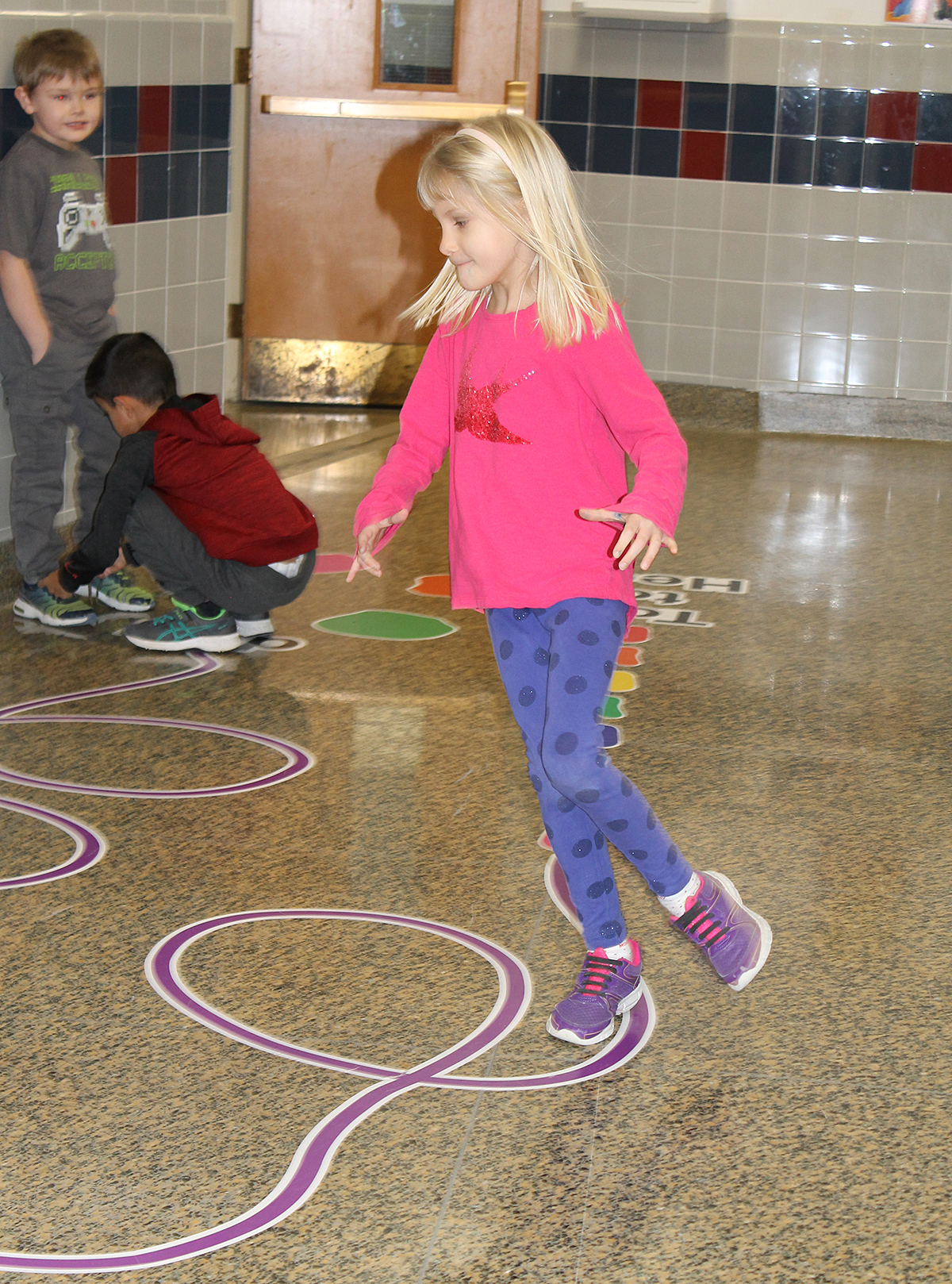 Students smiling as they walk on sticker path in hallway.