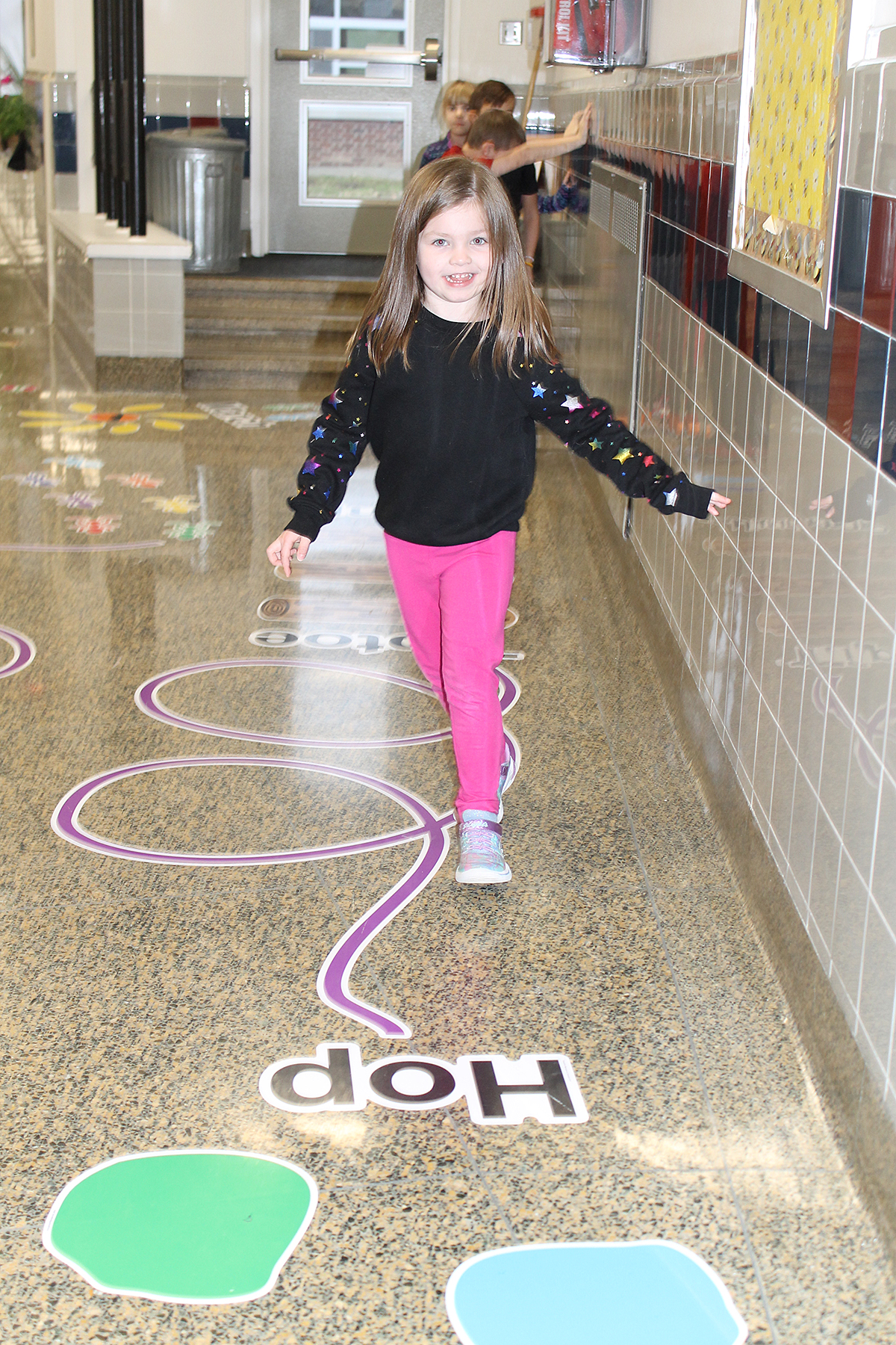 Student smmiling as she walks on sticker path in hallway.