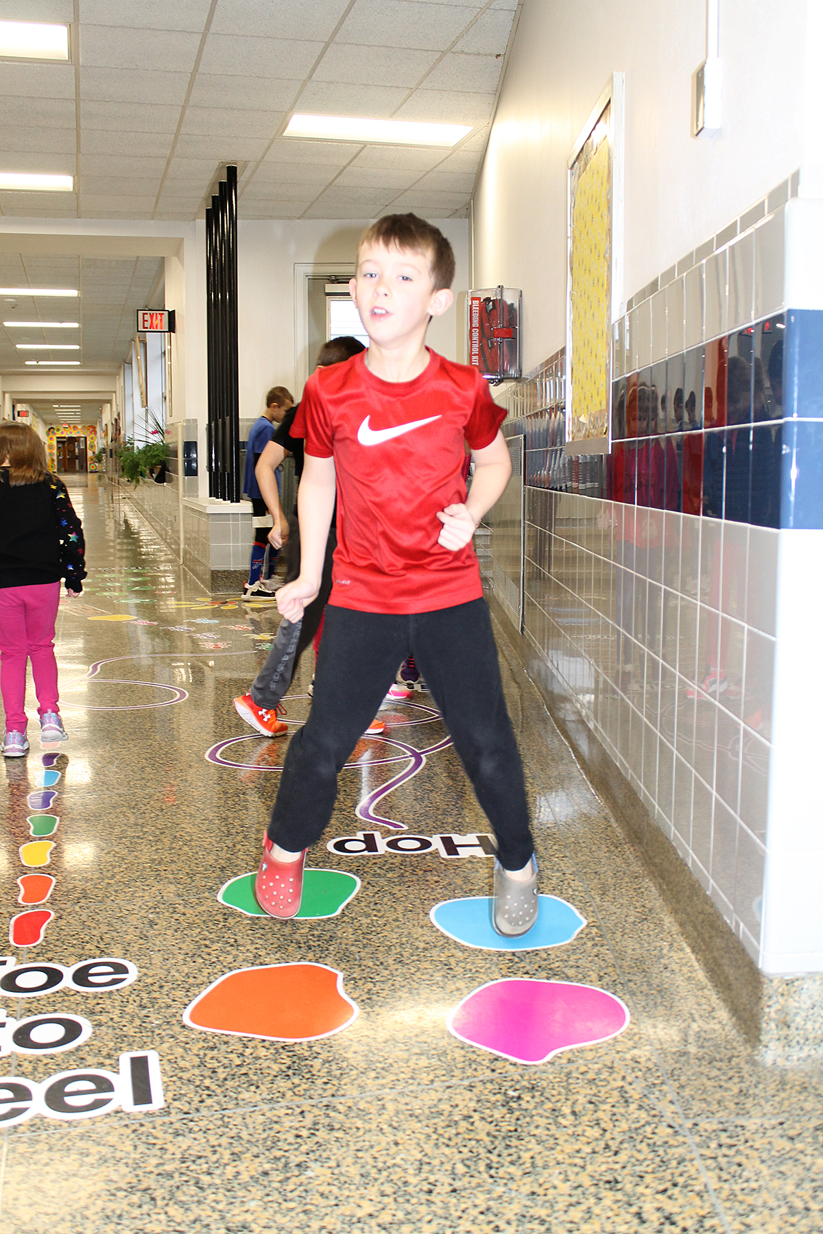 Student jumping along sticker path in hallway.