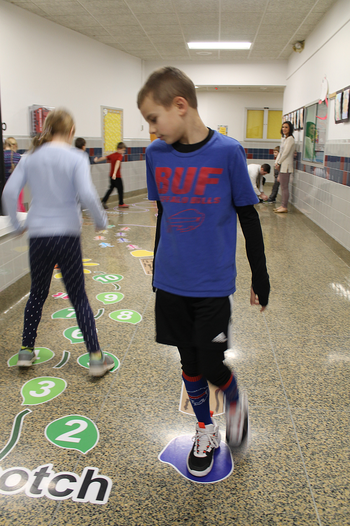 Two students walking on sticker path in hallway.