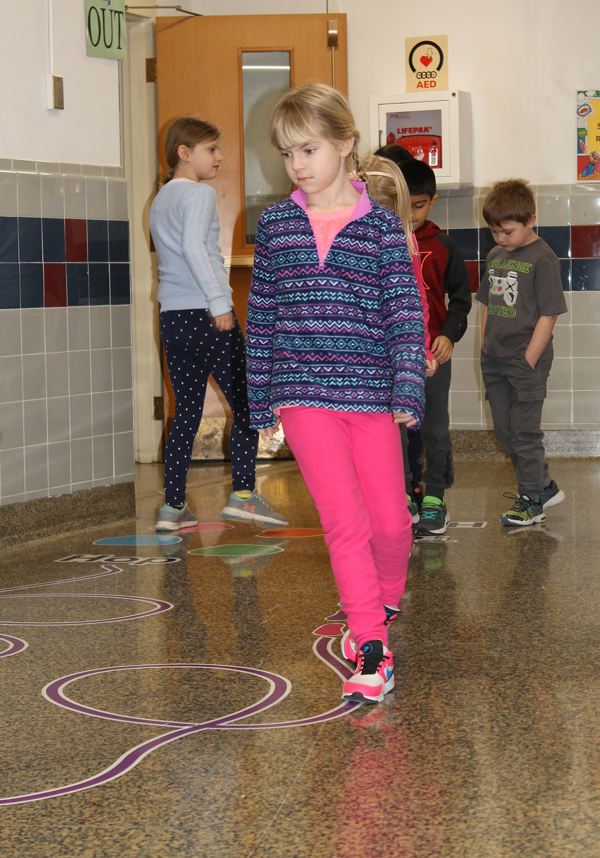 Students walking along sticker path in hallway.