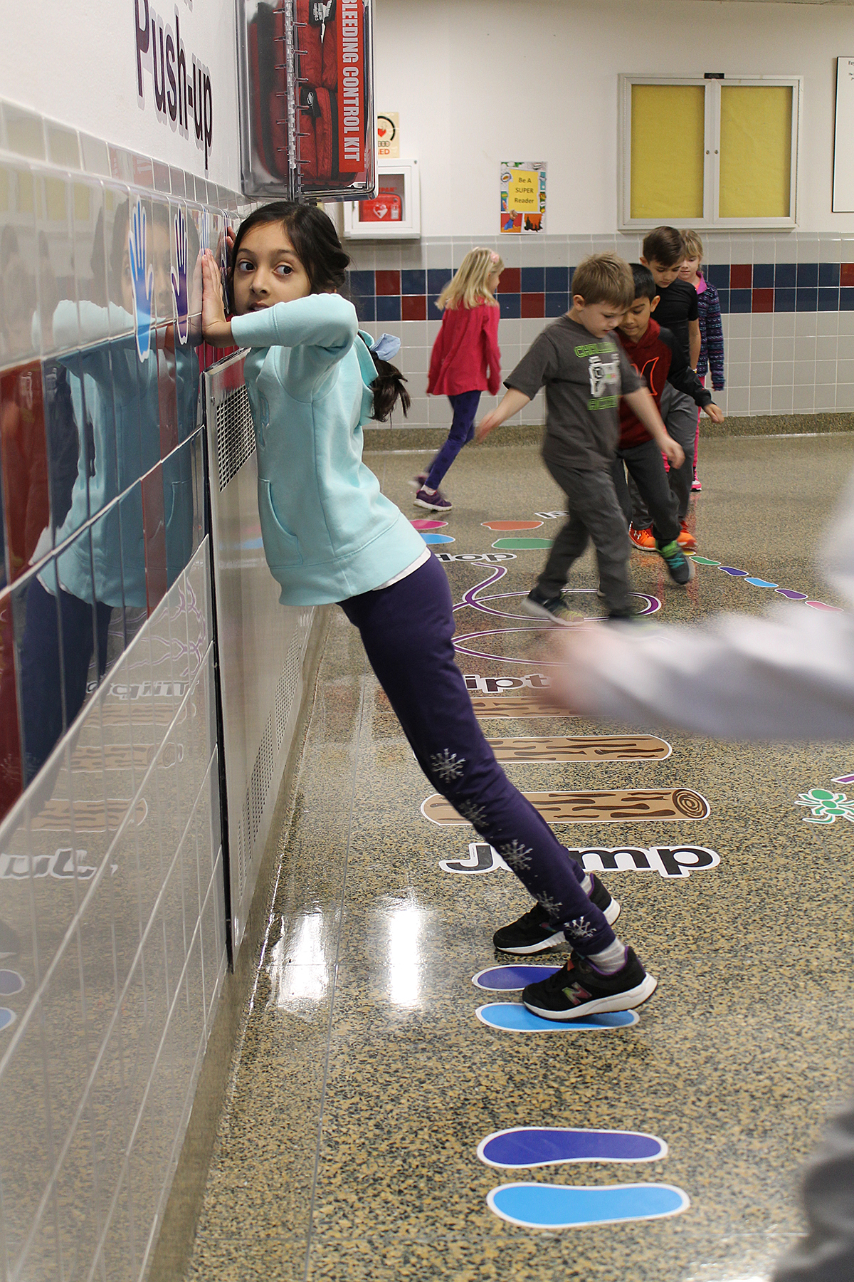 Students walking on sticker path in hallway.