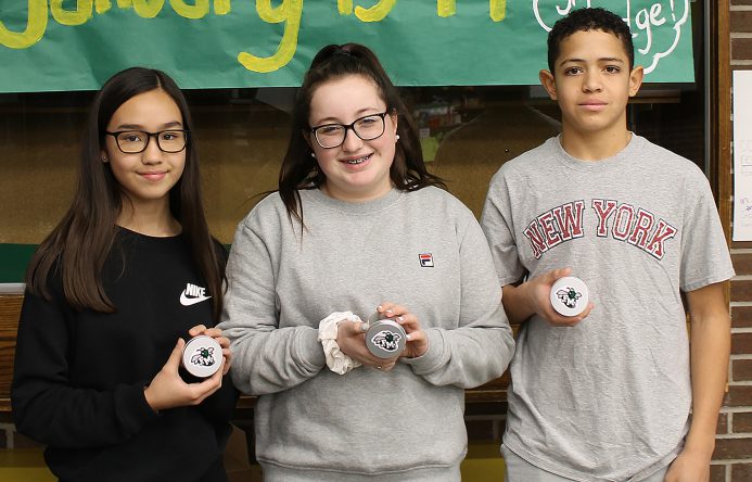 Three students standing side-by-side holding smalll silver canisters.