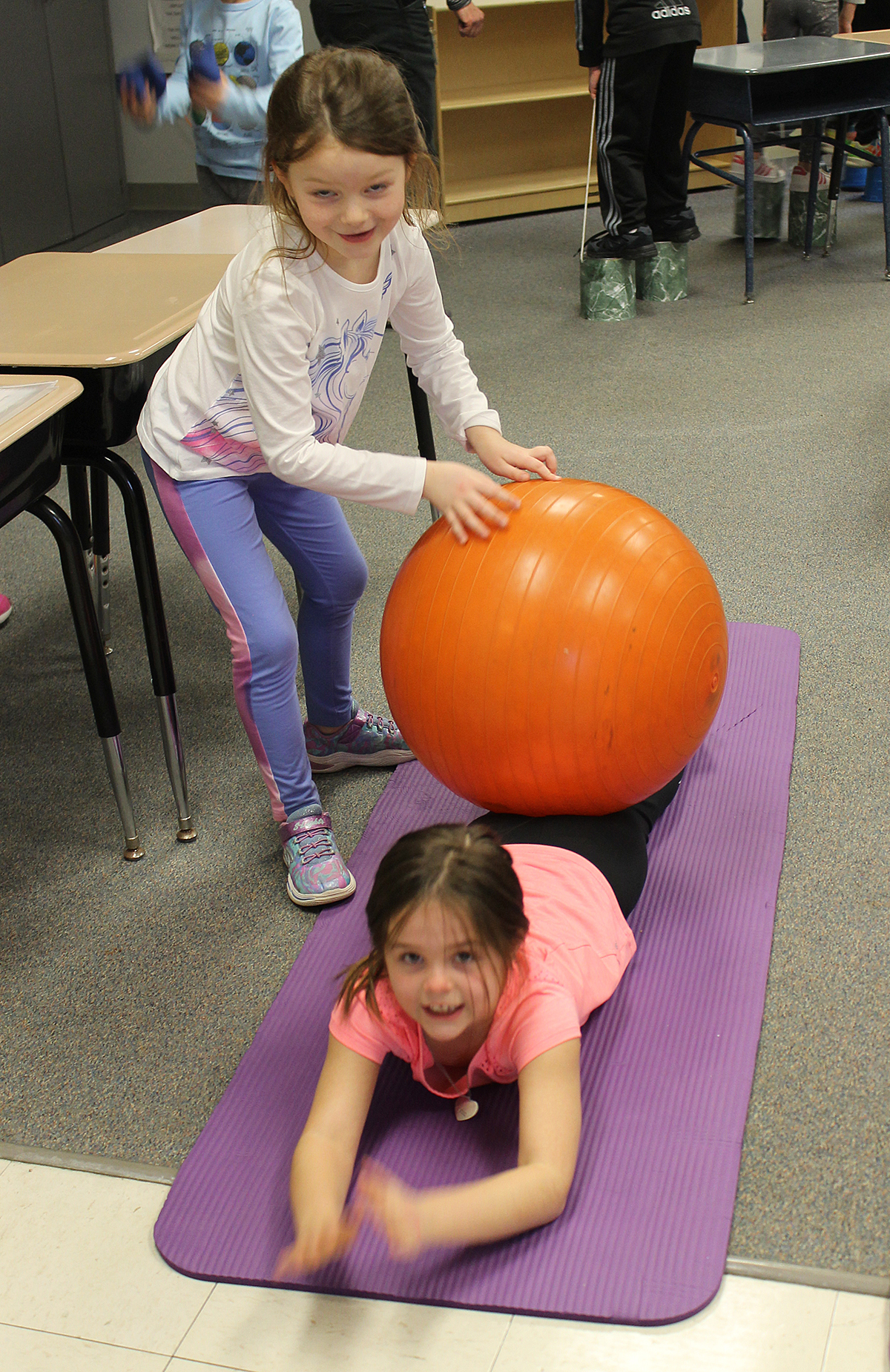 Girl rolling a large exercise ball on another girls back.