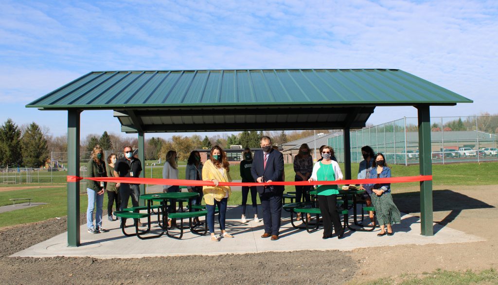 Group of people under pavilion with red ribbon stretched across the pavilion.