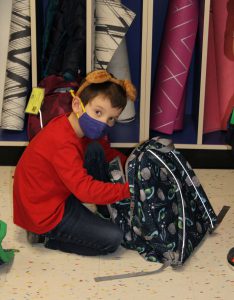 Student kneeling next to backpack, wearing a headband with brown bear ears. 