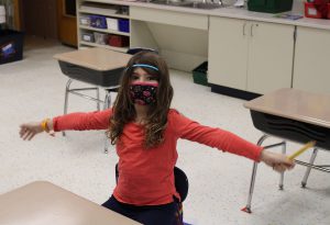 Student seated at desk holding arms outstretched. 