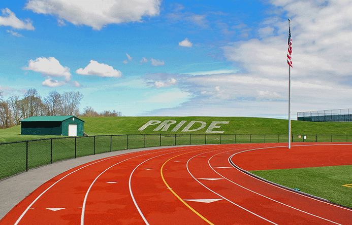 This is an image of the a running track and a grassy hill with the word "pride" chalked onto it.