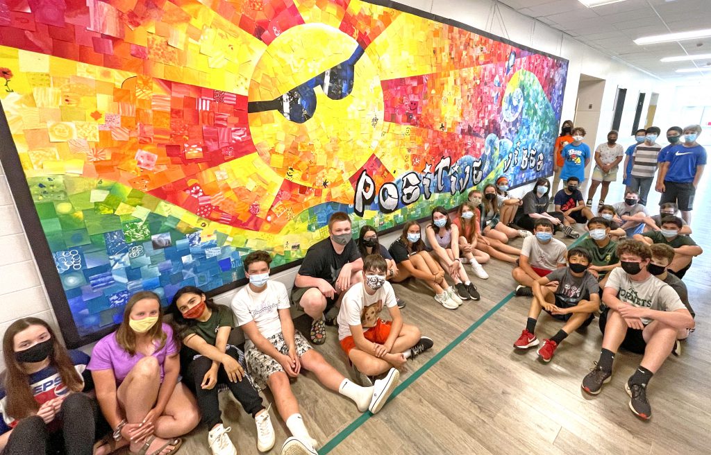 This is an image of an art mural on the wall and several students sitting in front of it.