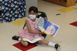 Student seated on floor holding up a book.