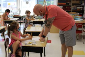 Teacher leaning on student's desk; student looking up at teacher.