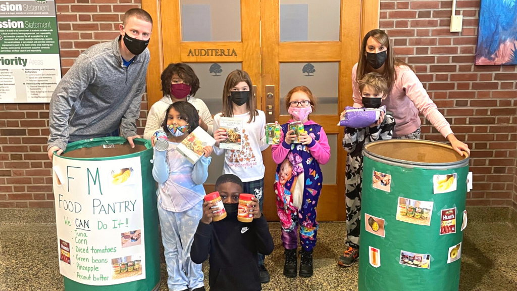 This is an image of two staff members and several students standing next to canned drive collection bins at school.