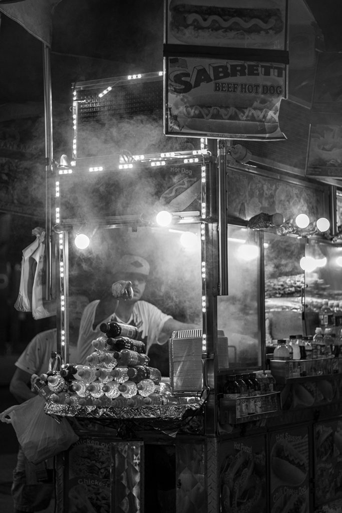 A street food vendor is surrounded by smoke and pointing at the viewer.