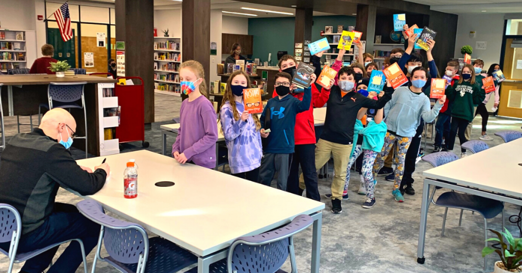 This is an image of author Gordon Korman autographing a book and students waiting in line