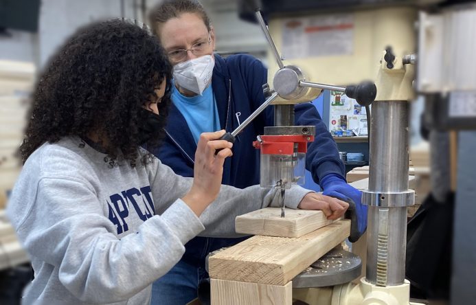 A student using a drill while receiving guidance from an instructor.