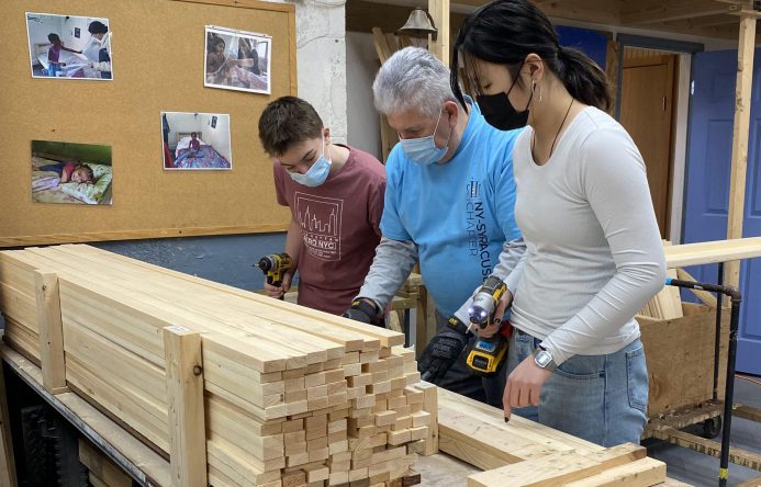 Three individuals working together to prepare wood.