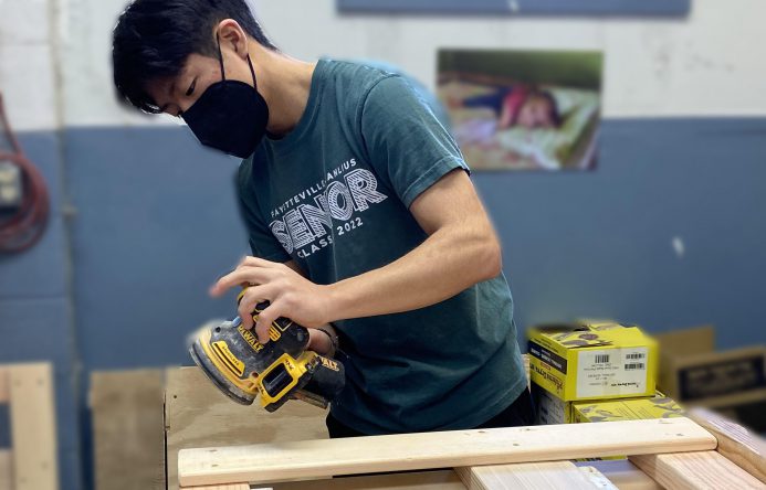 This is an image of a student using a sander on a piece of wood