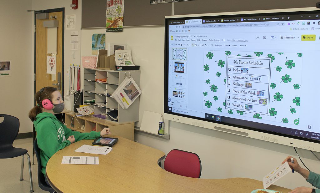 Stuent seated at table looking at image projected on a white board.