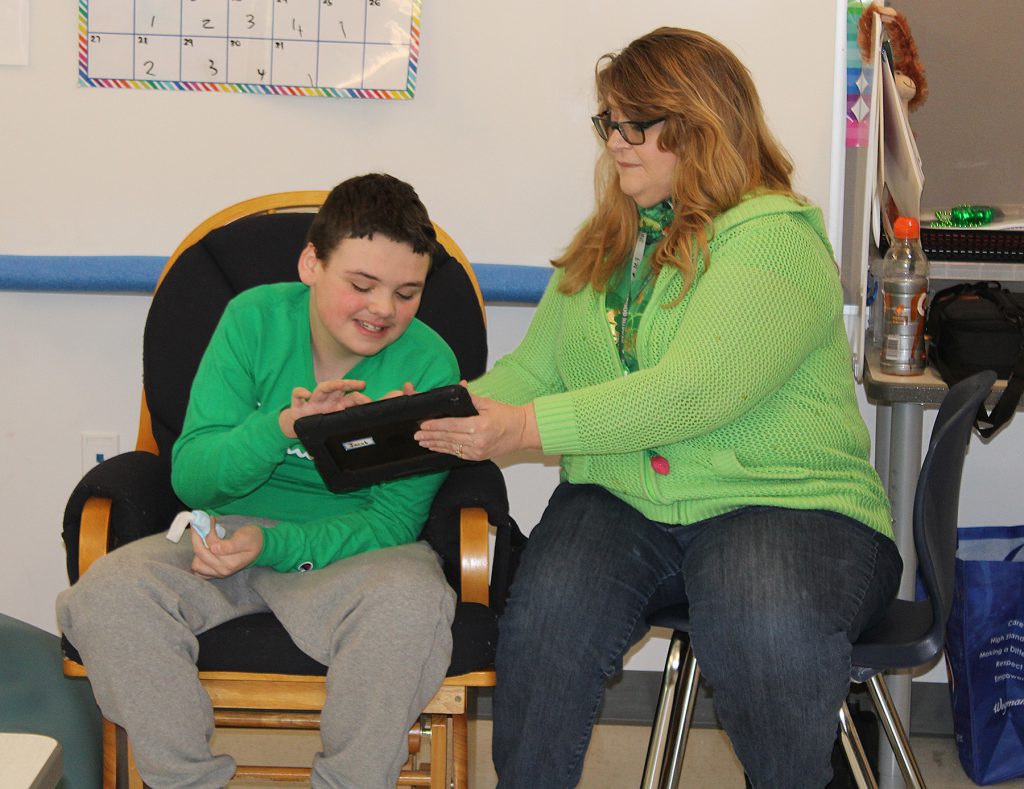Teacher holding an iPad while a student uses it.