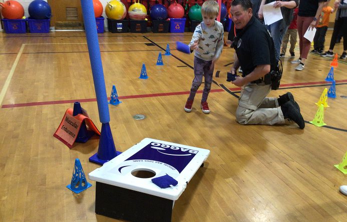 An adult helps a student toss a bean bag.