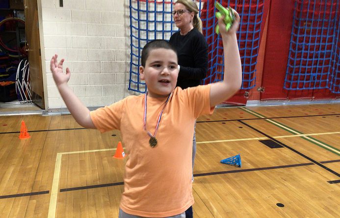 A student wearing a medal raises both arms in the air.