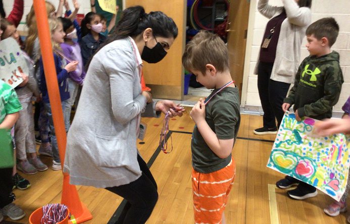 An adult hangs a medal around a student's neck.